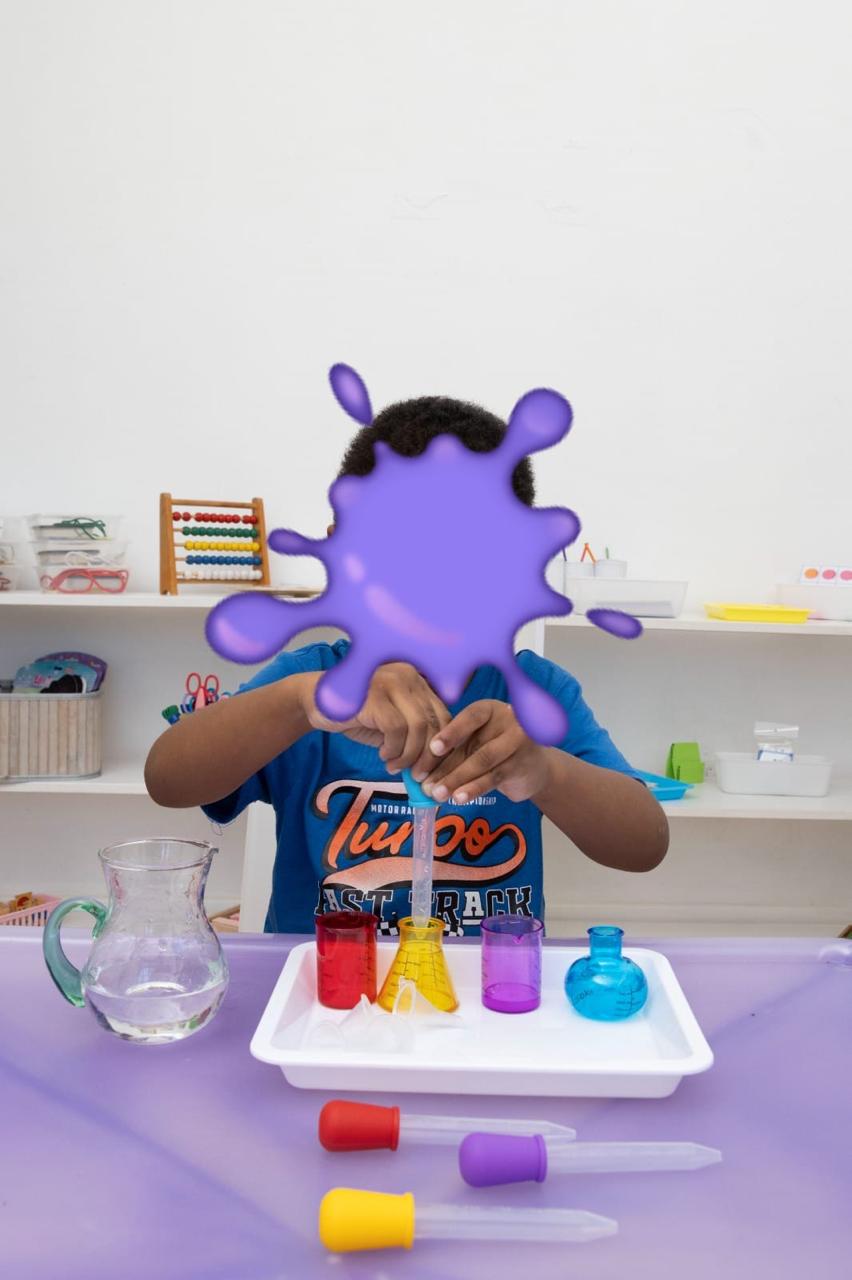 Child conducts a science experiment, pouring colored liquids into beakers on a tray at a classroom table.