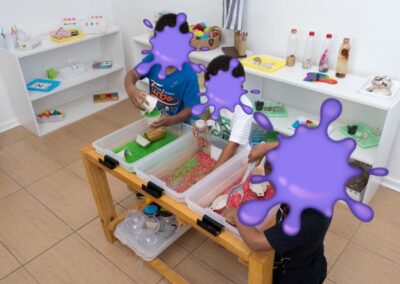 Children explore a sensory table filled with green and red rice and small tools in a bright classroom.